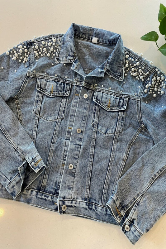 Denim jacket with pearl embellishments on a beige surface