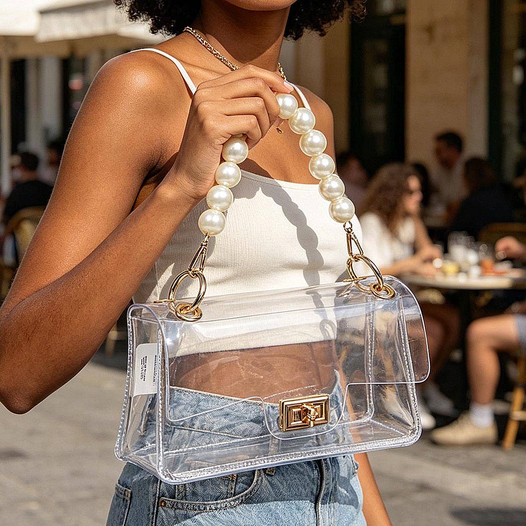 Person holding a clear handbag with a pearl handle in an outdoor setting