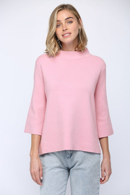 Woman wearing a pink top and light gray pants on a white background