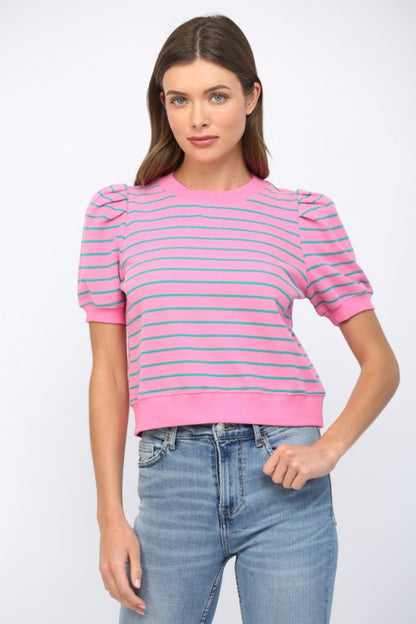 A woman modeling a pink short-sleeve knit top with thin blue horizontal stripes and puffed shoulders, paired with light-wash blue jeans against a light gray studio background.