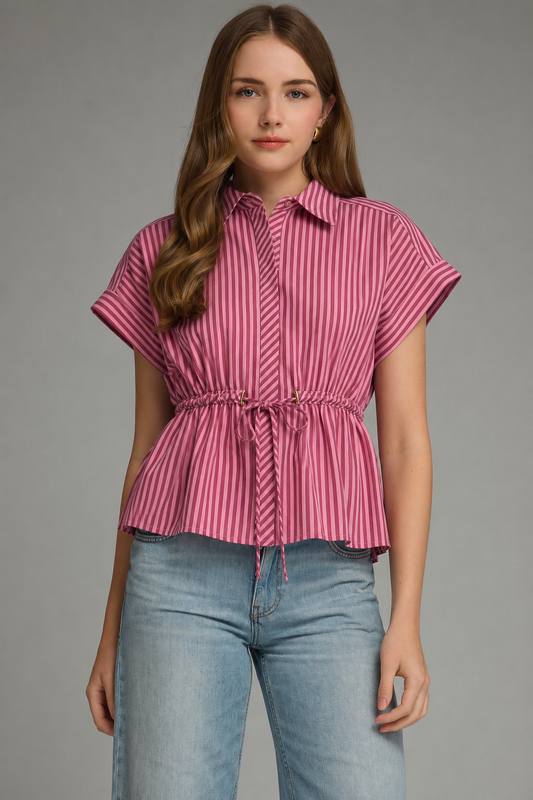 A woman modeling a pink and red vertically striped short-sleeve blouse with a drawstring waist, paired with light blue jeans, against a solid gray studio background.