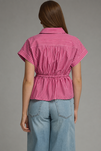 A woman shown from the back wearing a pink and red vertically striped short-sleeve top with a gathered waist, paired with light blue jeans, against a solid gray studio background.