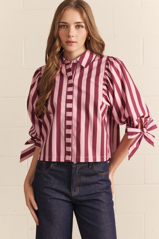 Woman wearing a red and white striped blouse with tied sleeves against a light background