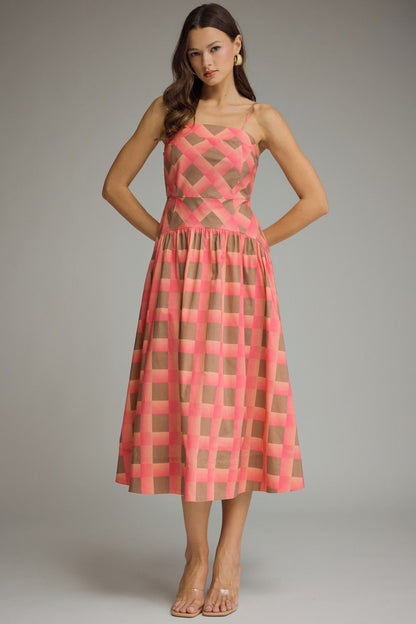 A woman modeling a sleeveless midi dress with a pink and green geometric pattern, standing against a neutral gray studio background.