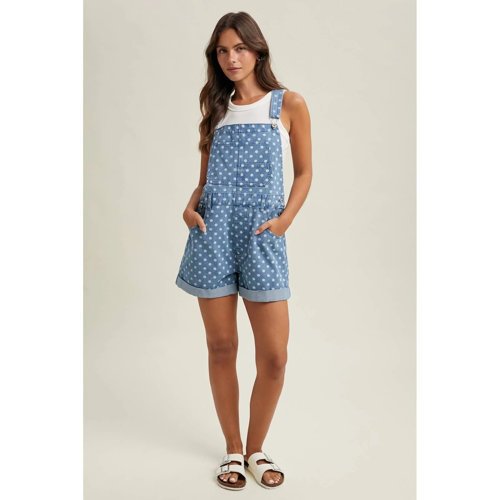 Woman wearing a blue polka dot overalls with a white top on a beige background