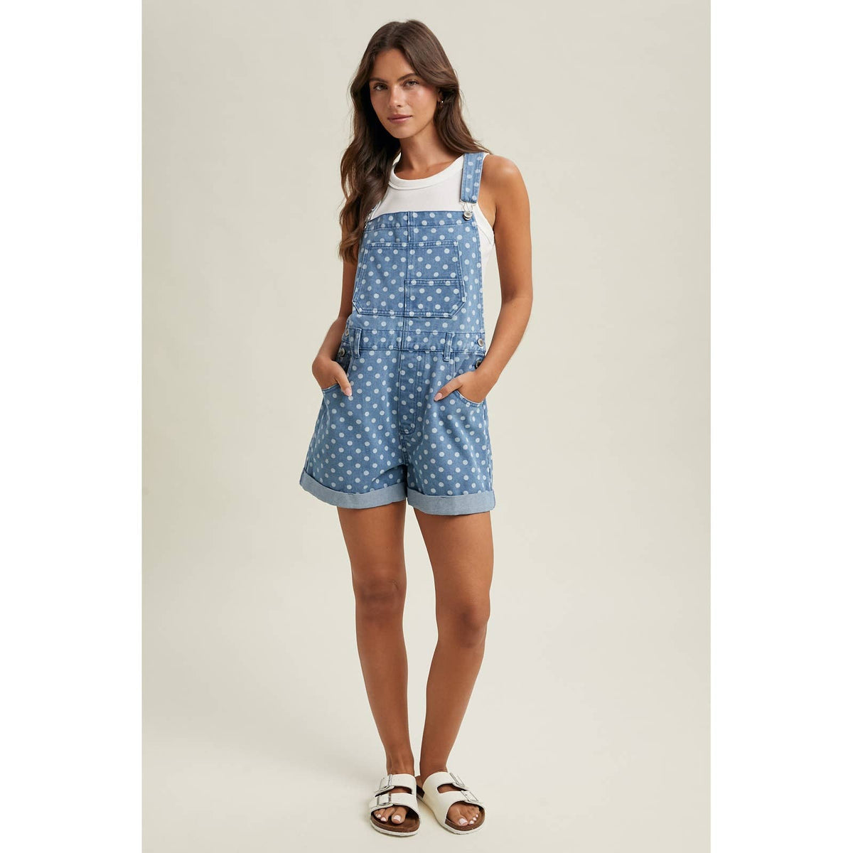 Woman wearing a blue polka dot overalls with a white top on a beige background