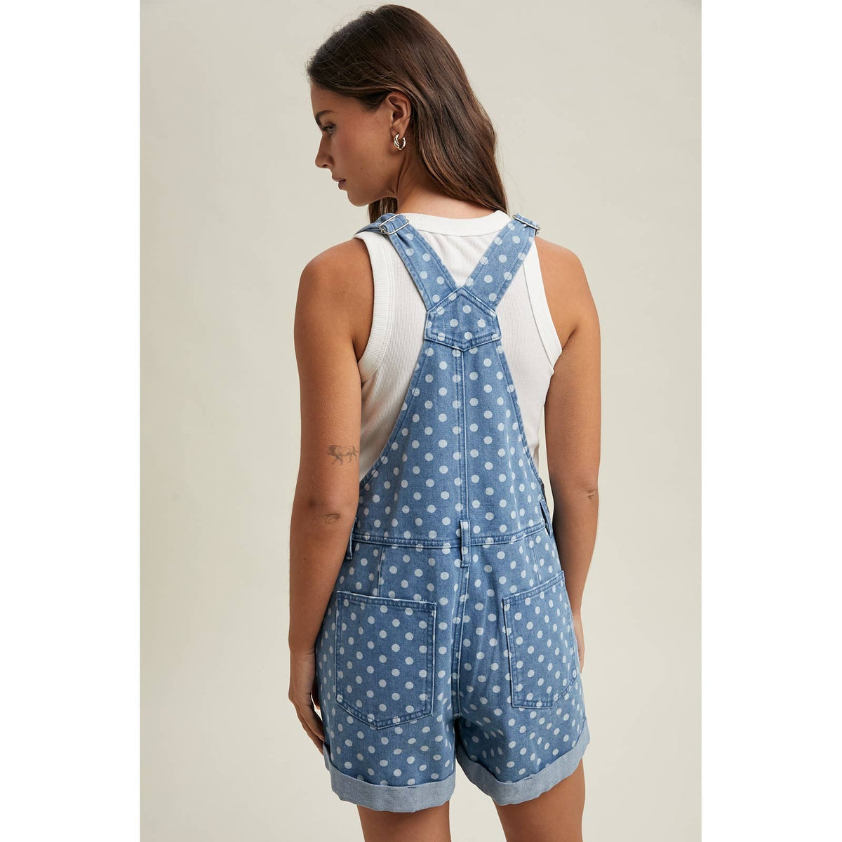 Woman wearing a blue polka dot denim overall dress on a neutral background