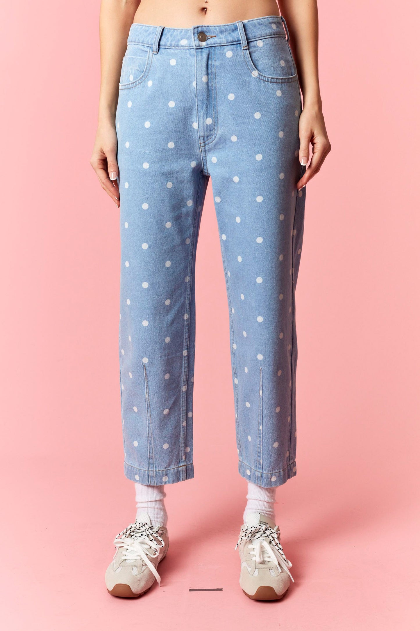 Light blue jeans with white polka dots worn by a person on a pink background