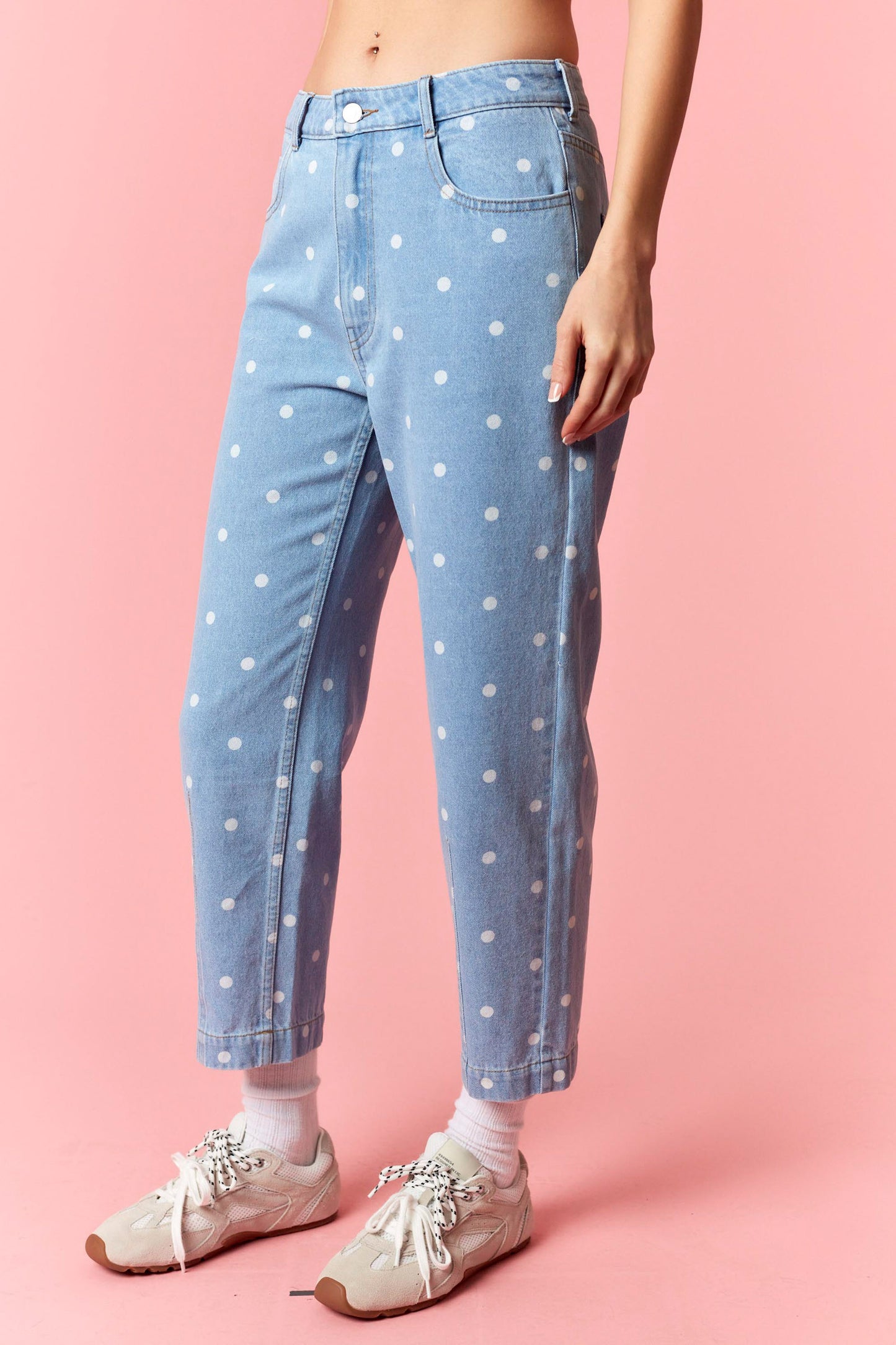 Person wearing light blue jeans with white polka dots on a pink background