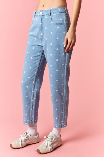 Person wearing light blue jeans with white polka dots on a pink background