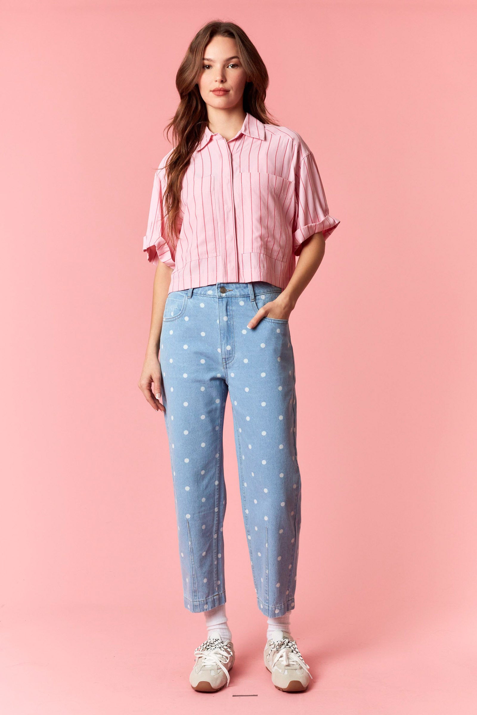 Woman wearing a pink striped shirt and blue jeans with white polka dots on a pink background