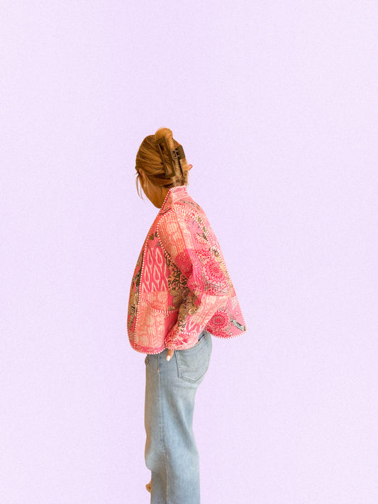 A person shown from the back wearing a pink patterned cropped jacket and light blue jeans against a solid light purple background.