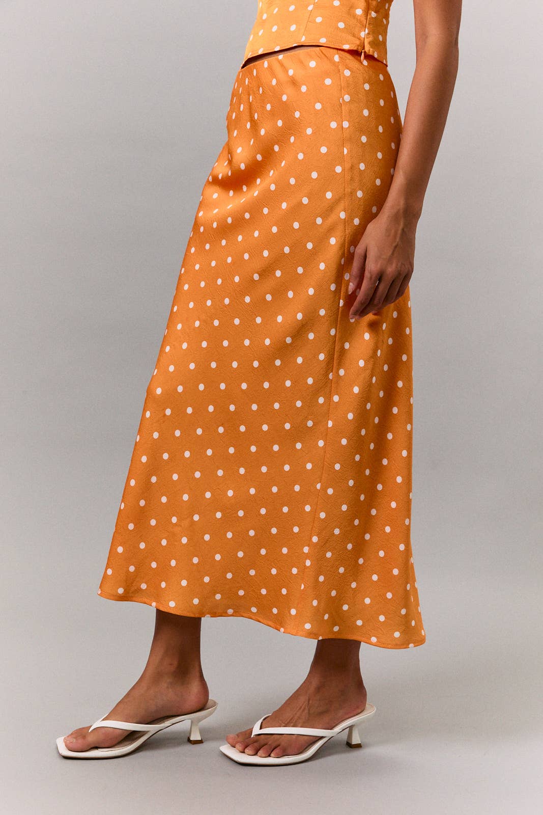 Person wearing an orange polka dot dress on a gray background
