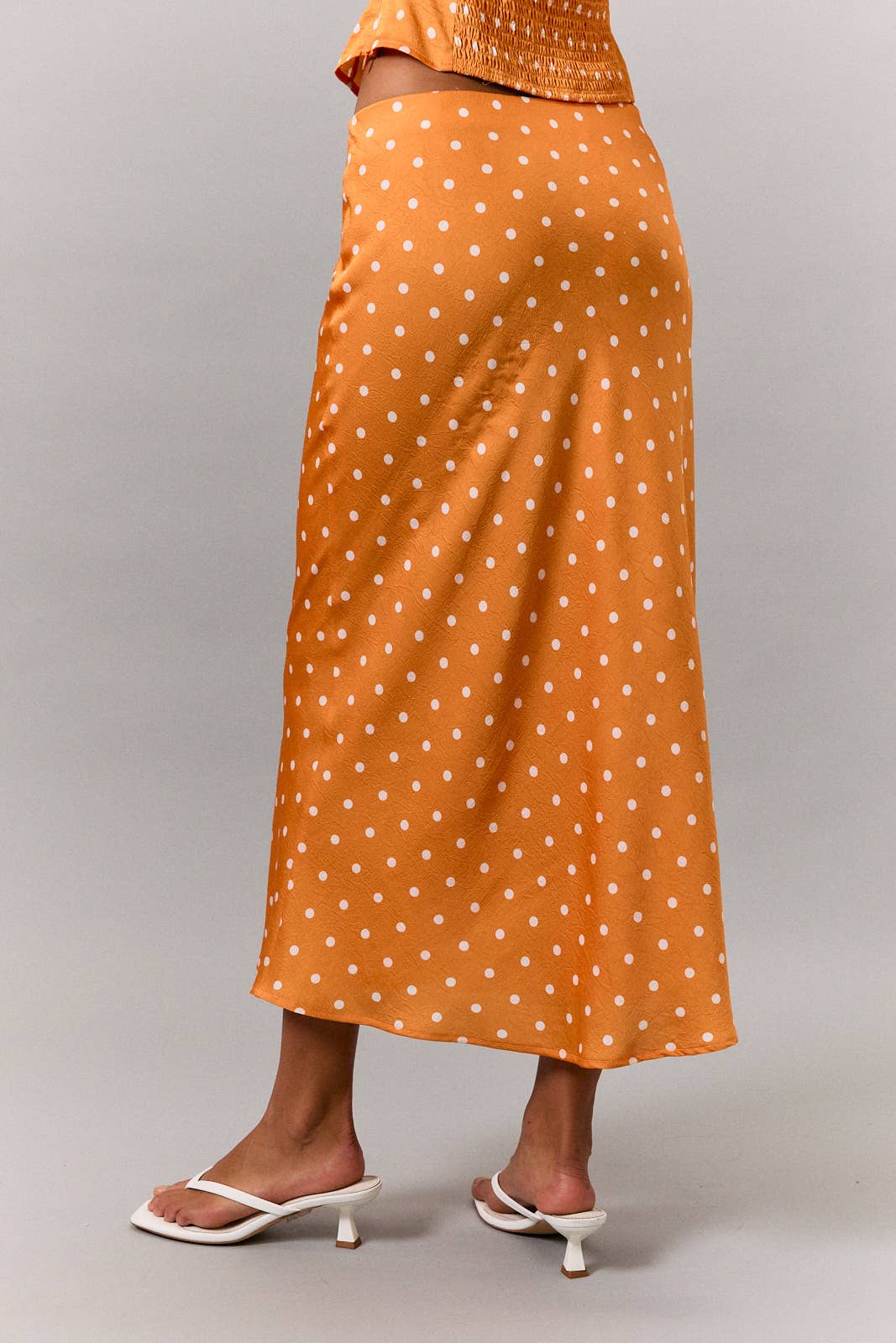 Orange polka dot skirt worn by a person on a gray background
