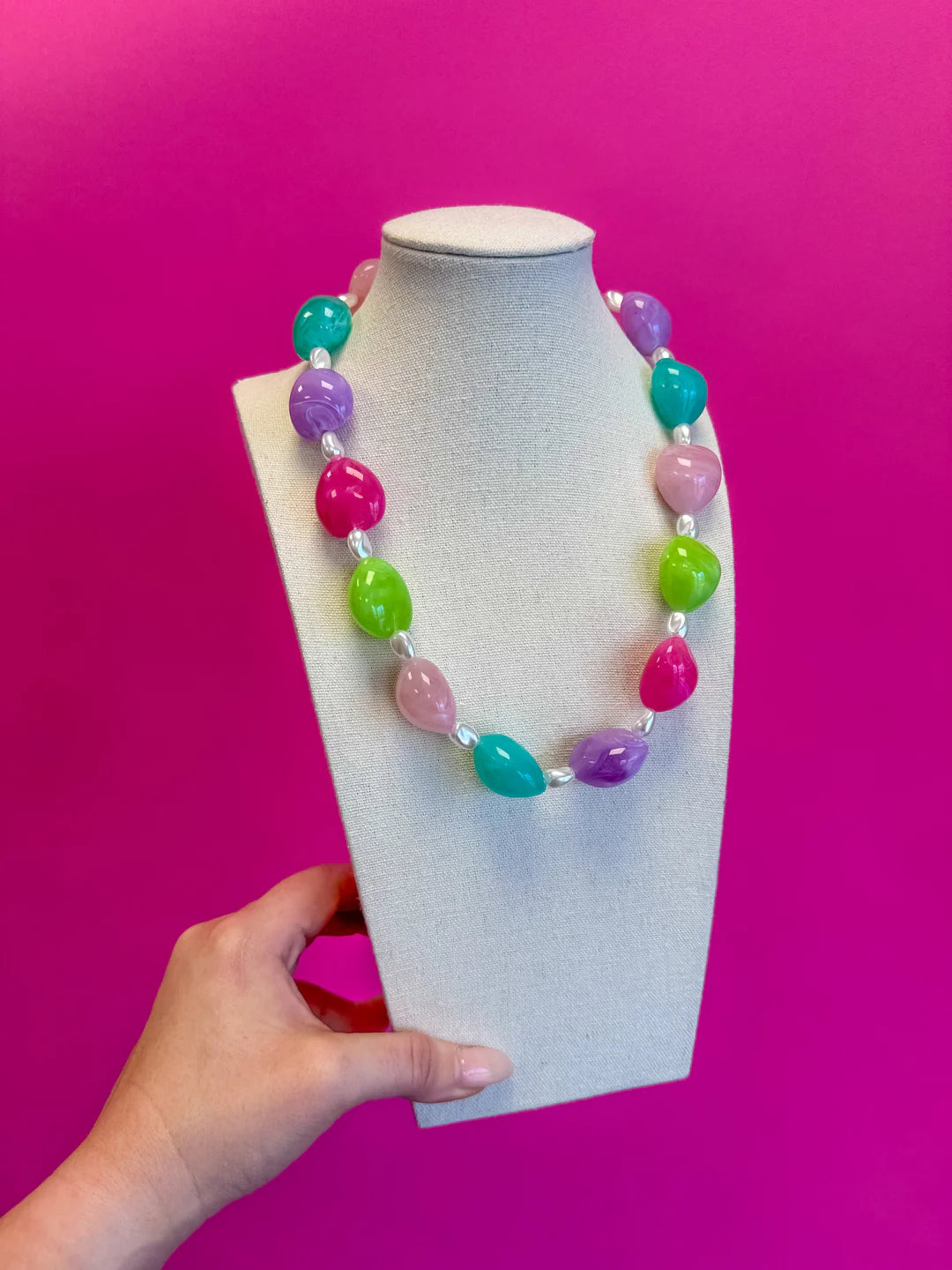 Colorful beaded necklace on a mannequin bust against a pink background