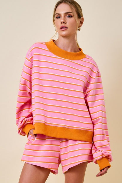A woman modeling a pink and orange striped sweatshirt and matching shorts set against a solid beige background.