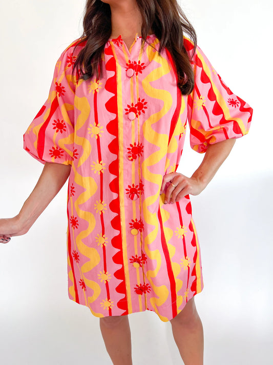 Woman wearing a colorful patterned dress with red, yellow, and pink design on a white background