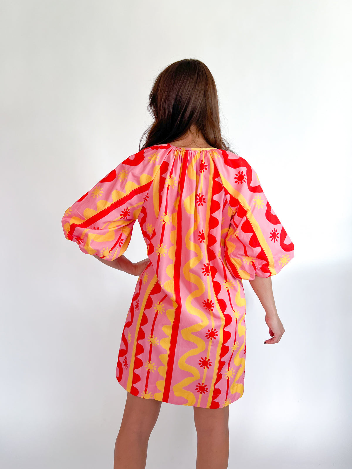 Woman wearing a colorful dress with red, yellow, and pink patterns on a white background