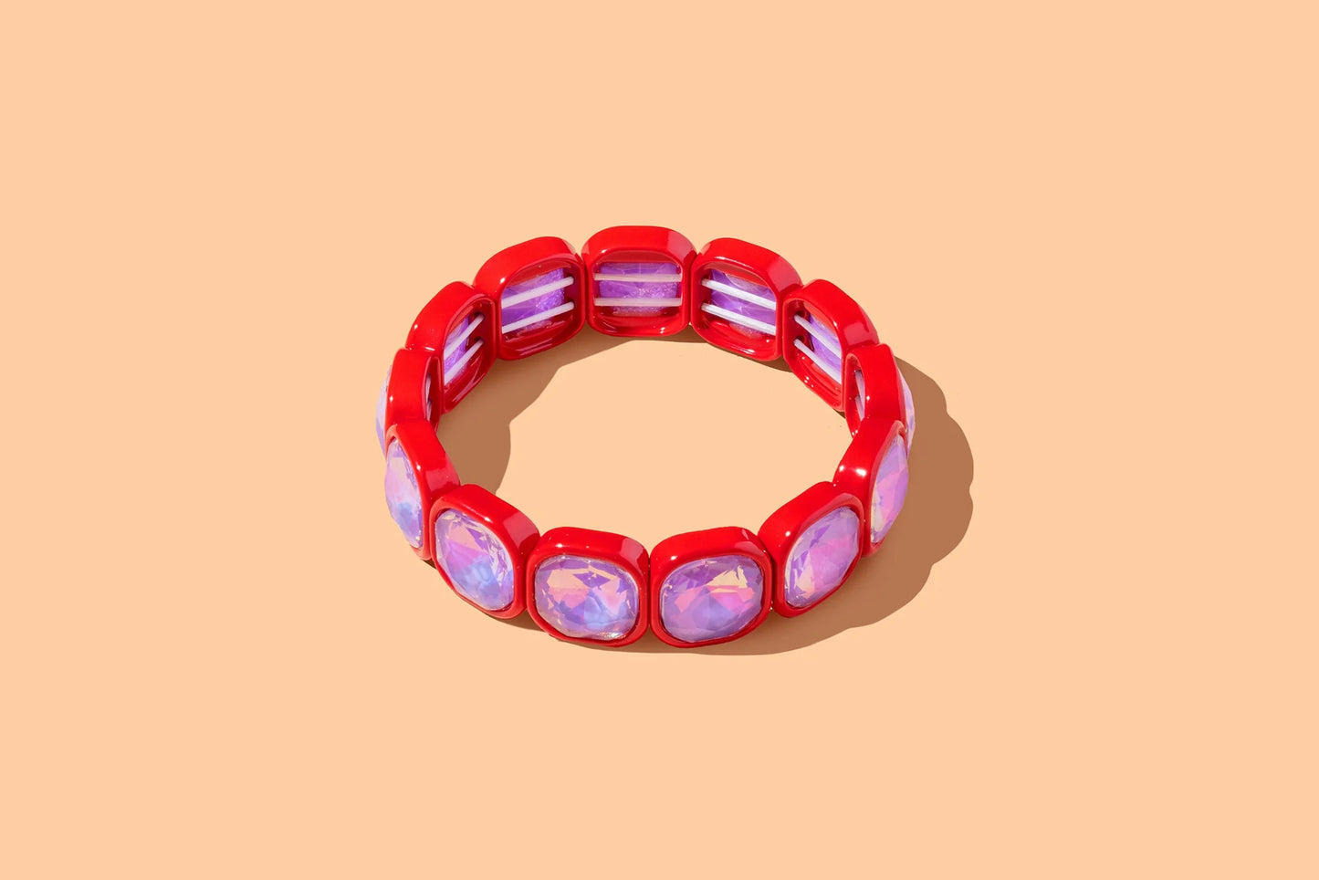 Red stretch bracelet with iridescent pink gemstones on a solid peach background