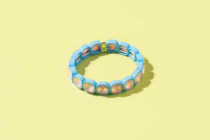 Blue stretch bracelet with iridescent square crystals on a pastel yellow background