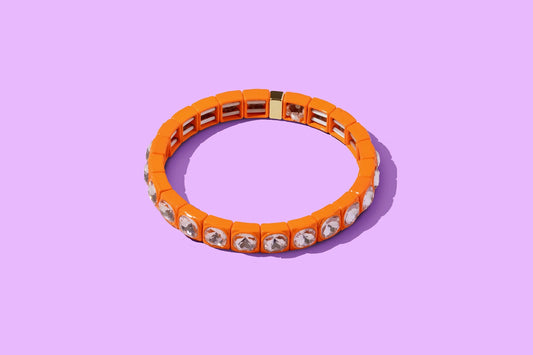 Orange stretch bracelet with clear crystal accents on a purple background