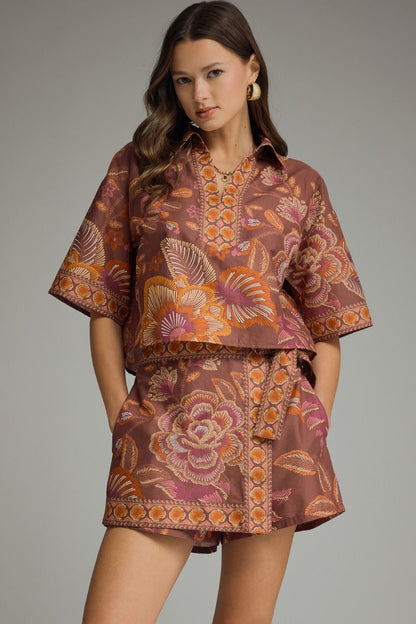 Model wearing terracotta floral two piece skort set with cropped collared top, decorative trim and matching wrap-front skort.