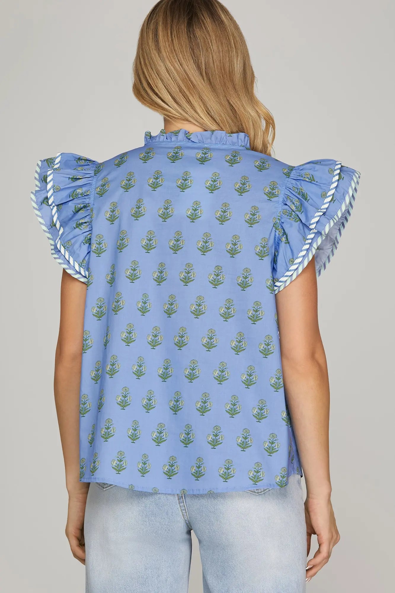 sky blue floral flutter sleeve blouse with green block print and ruffle neckline worn with light wash jeans.