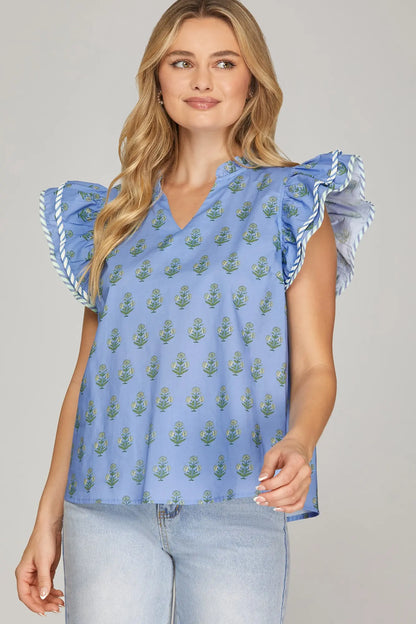 sky blue floral flutter sleeve blouse with green block print and ruffle neckline worn with light wash jeans.