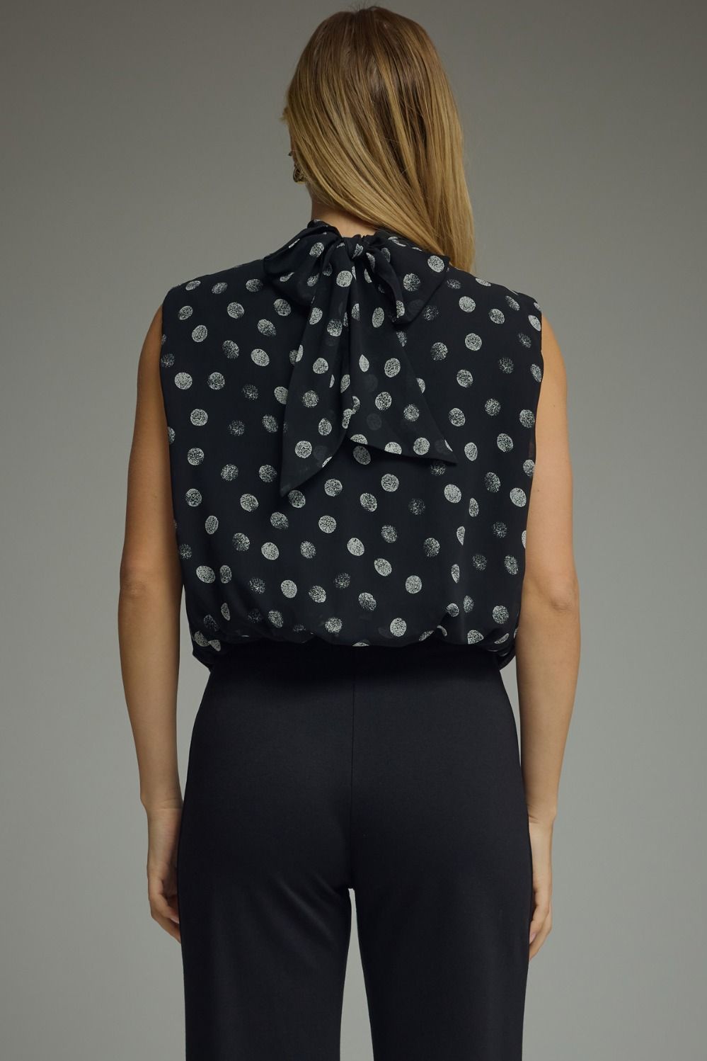 Woman wearing a black sleeveless top with white polka dots and black pants on a gray background