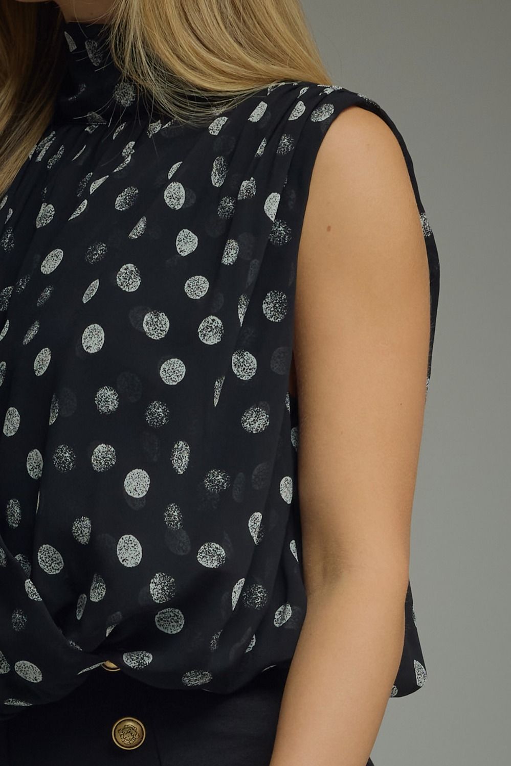 Black sleeveless top with white polka dot pattern worn by a person on a gray background