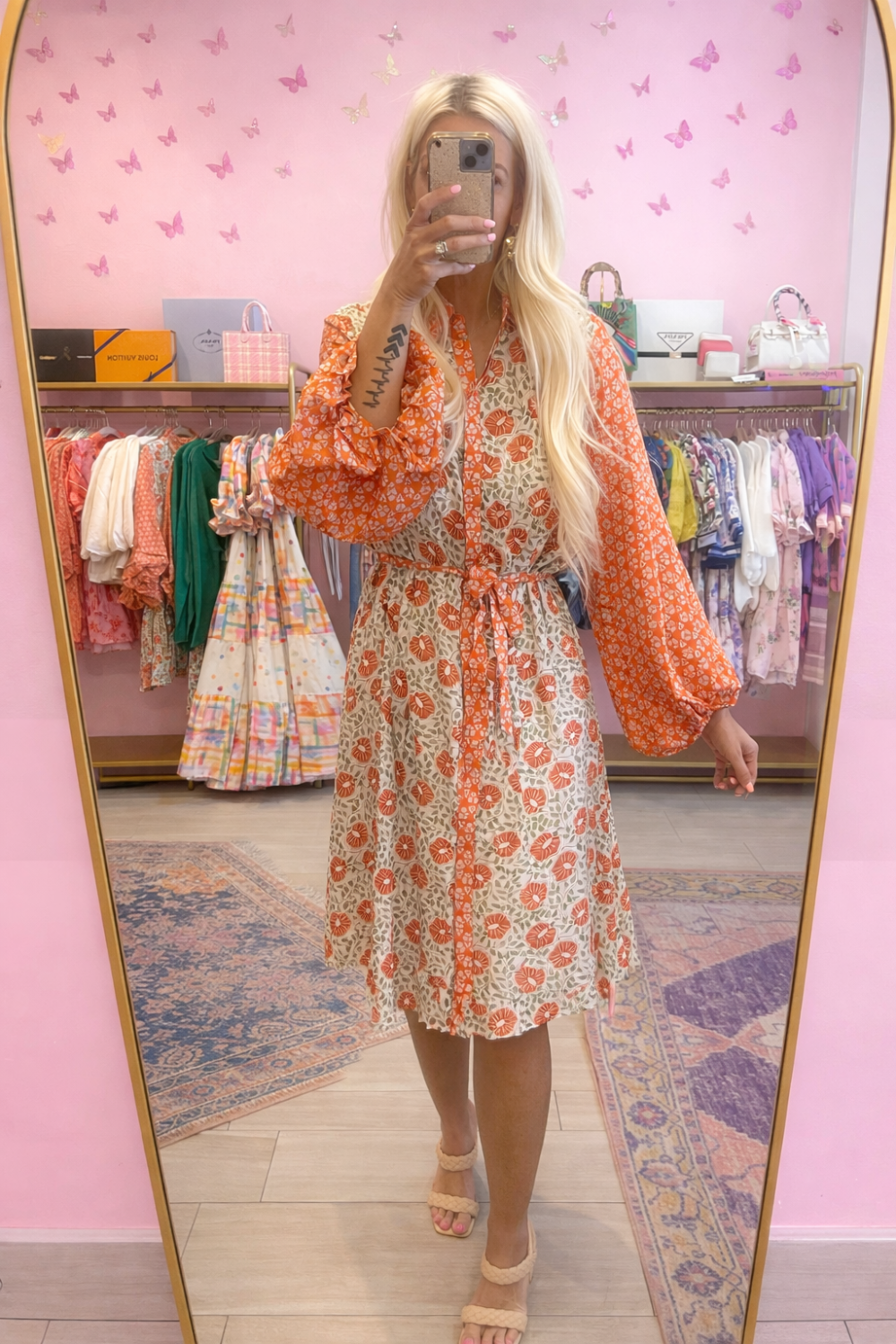 Person wearing an orange floral dress in a clothing store with pink walls and butterfly decorations.