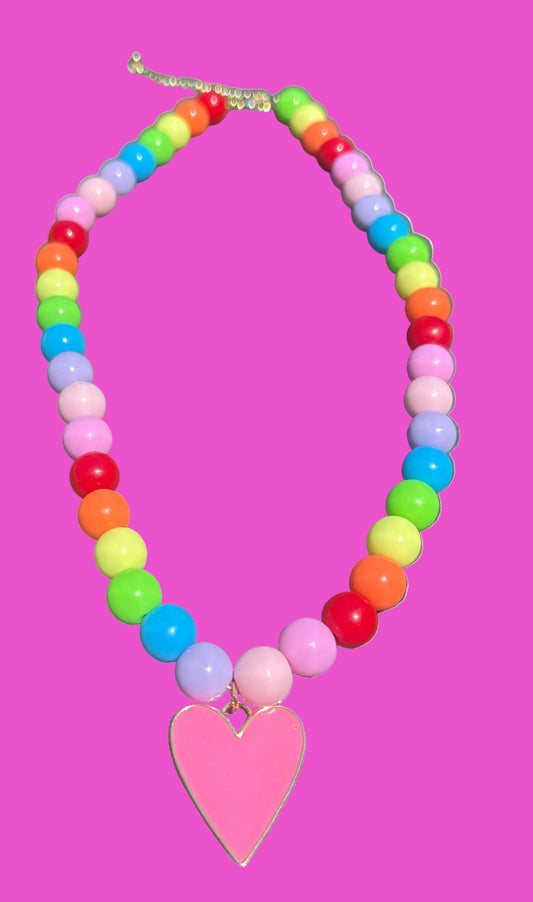 A colorful beaded necklace with rainbow-colored round beads and a pink heart-shaped pendant, displayed on a dark gray surface.