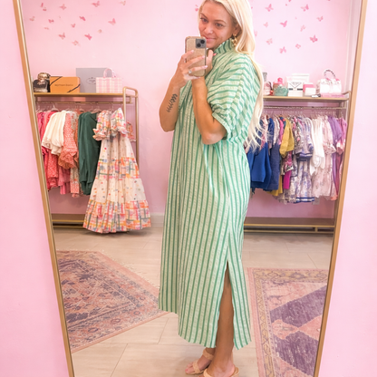 Woman taking a mirror selfie wearing a green striped dress in a clothing store.