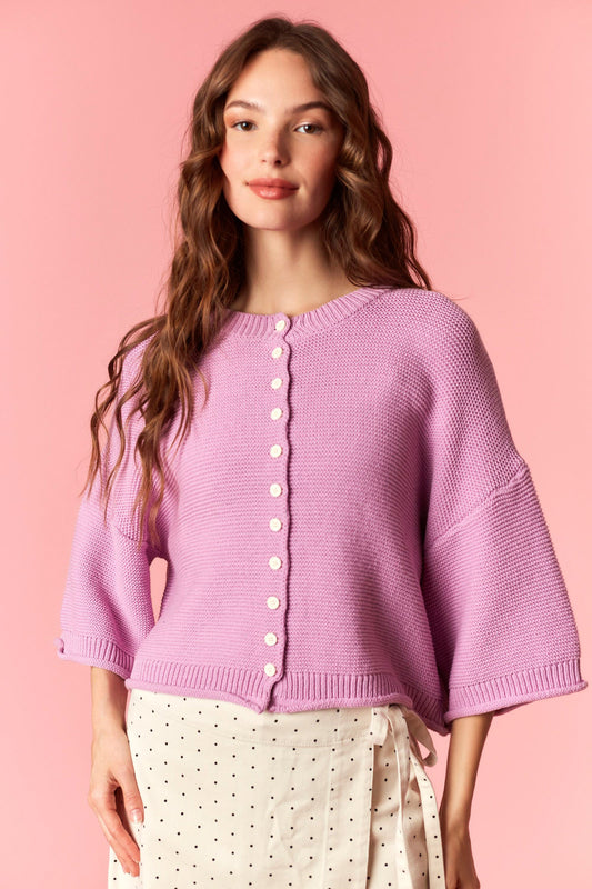 Woman wearing a light purple cardigan against a pink background 