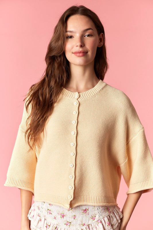 Woman wearing a beige knitted poncho against a pink background