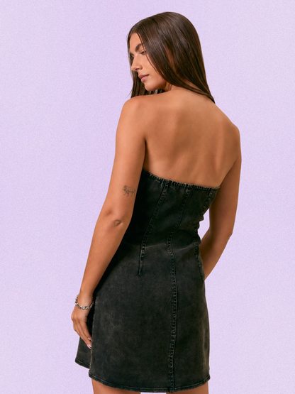 A woman shown from the back wearing a strapless black denim mini dress against a solid light purple background.