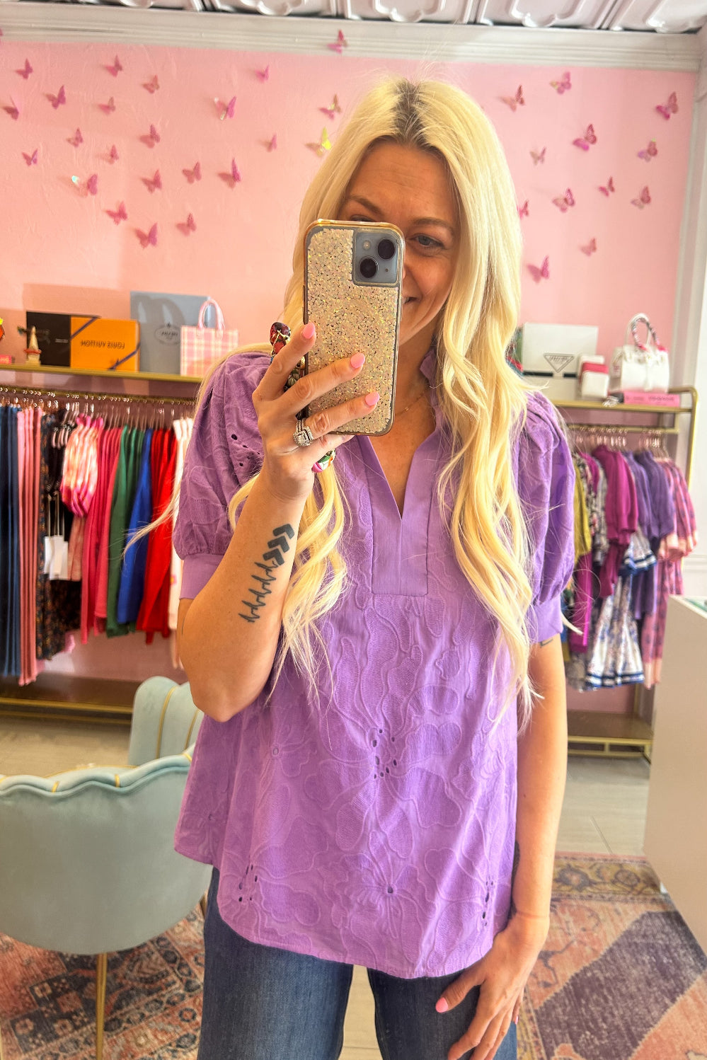 Person wearing a purple shirt taking a mirror selfie in a store with pink walls and clothing racks.