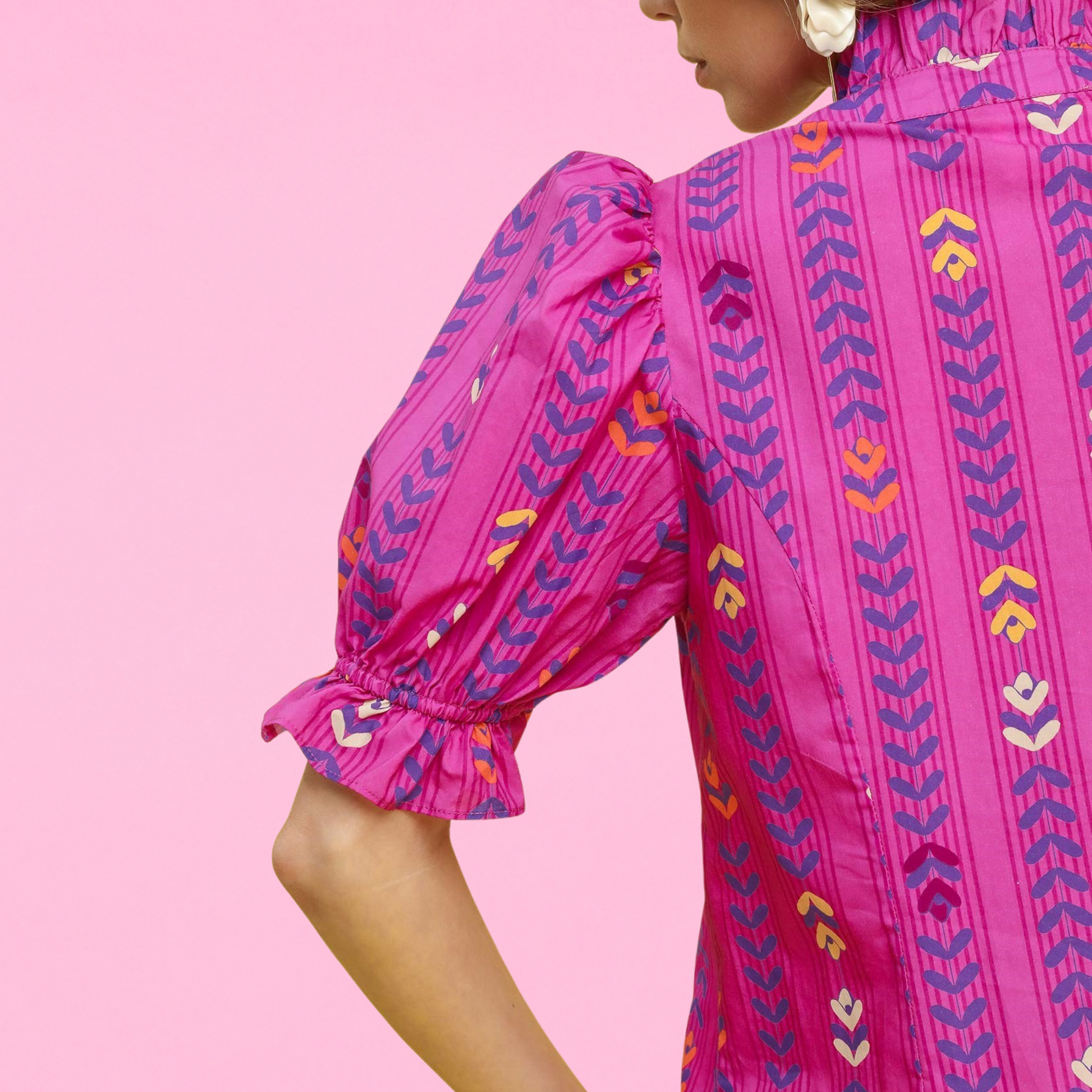 Close-up of a woman wearing a bright magenta blouse with puff sleeves and colorful geometric embroidery, showing ruffle cuff and back collar details.