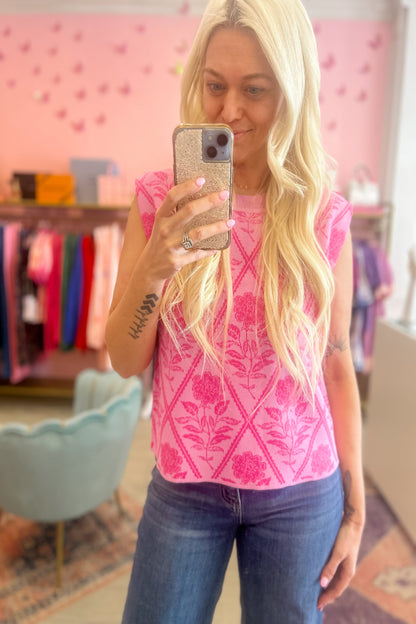 Woman taking a mirror selfie wearing a pink floral top and blue jeans in a store.