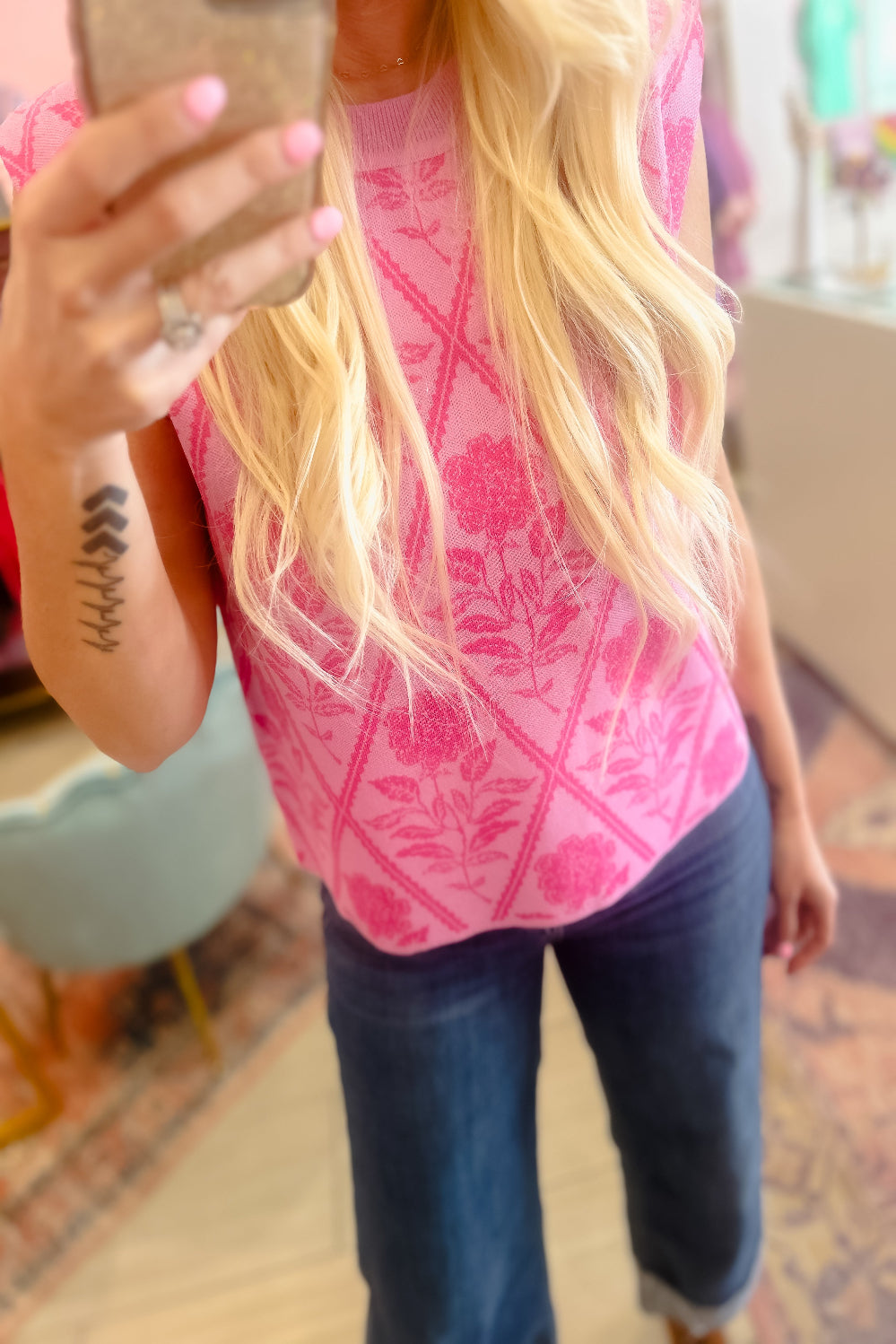 Person wearing a pink floral top and blue jeans taking a mirror selfie.