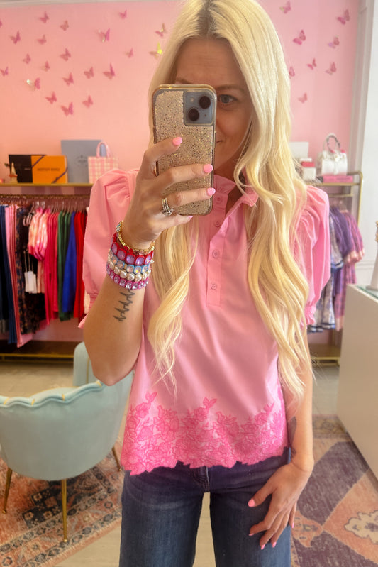Person wearing a pink blouse with lace details in a store setting.