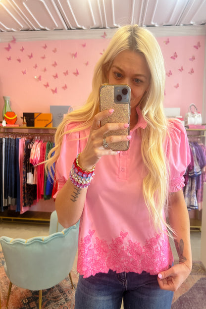 Woman taking a mirror selfie wearing a pink blouse with lace details in a store.
