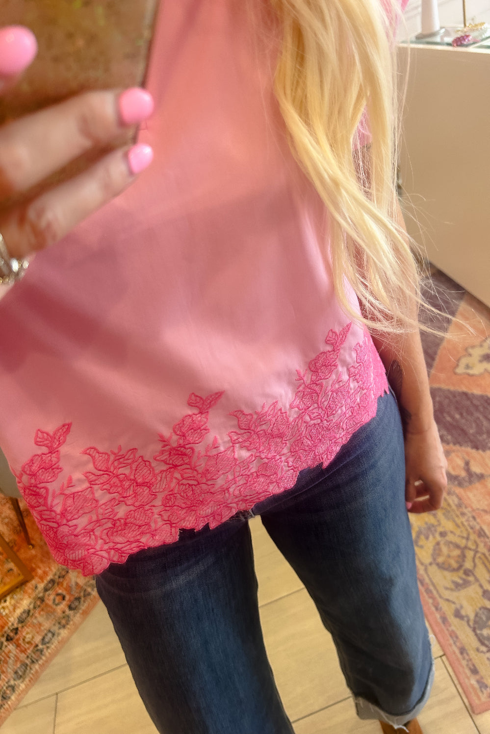 Person wearing a pink lace top and blue jeans indoors.