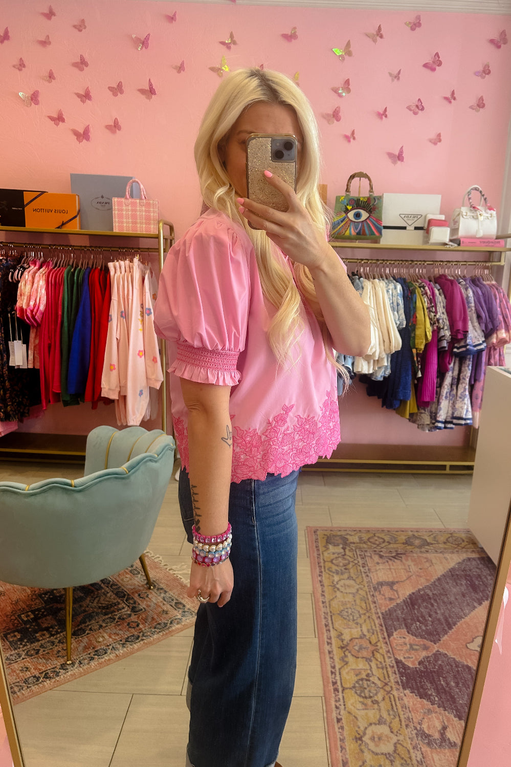Person wearing a pink blouse and blue jeans in a store with pink walls and butterfly decorations.