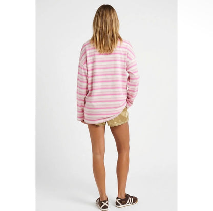 A woman viewed from behind wearing a pink and white striped long-sleeve t-shirt, gold patterned shorts, and brown sneakers against a light gray studio background.