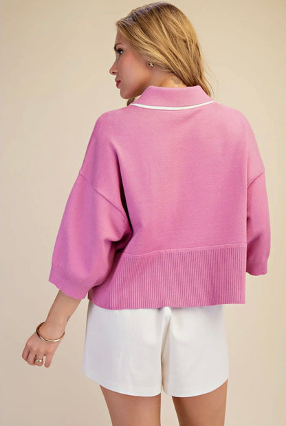 A woman shown from the back wearing a pink cropped knit sweater with white trim and white shorts, against a plain beige studio background.