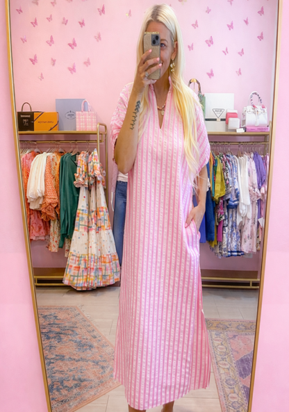 Woman taking a mirror selfie wearing a pink checkered dress in a clothing store.