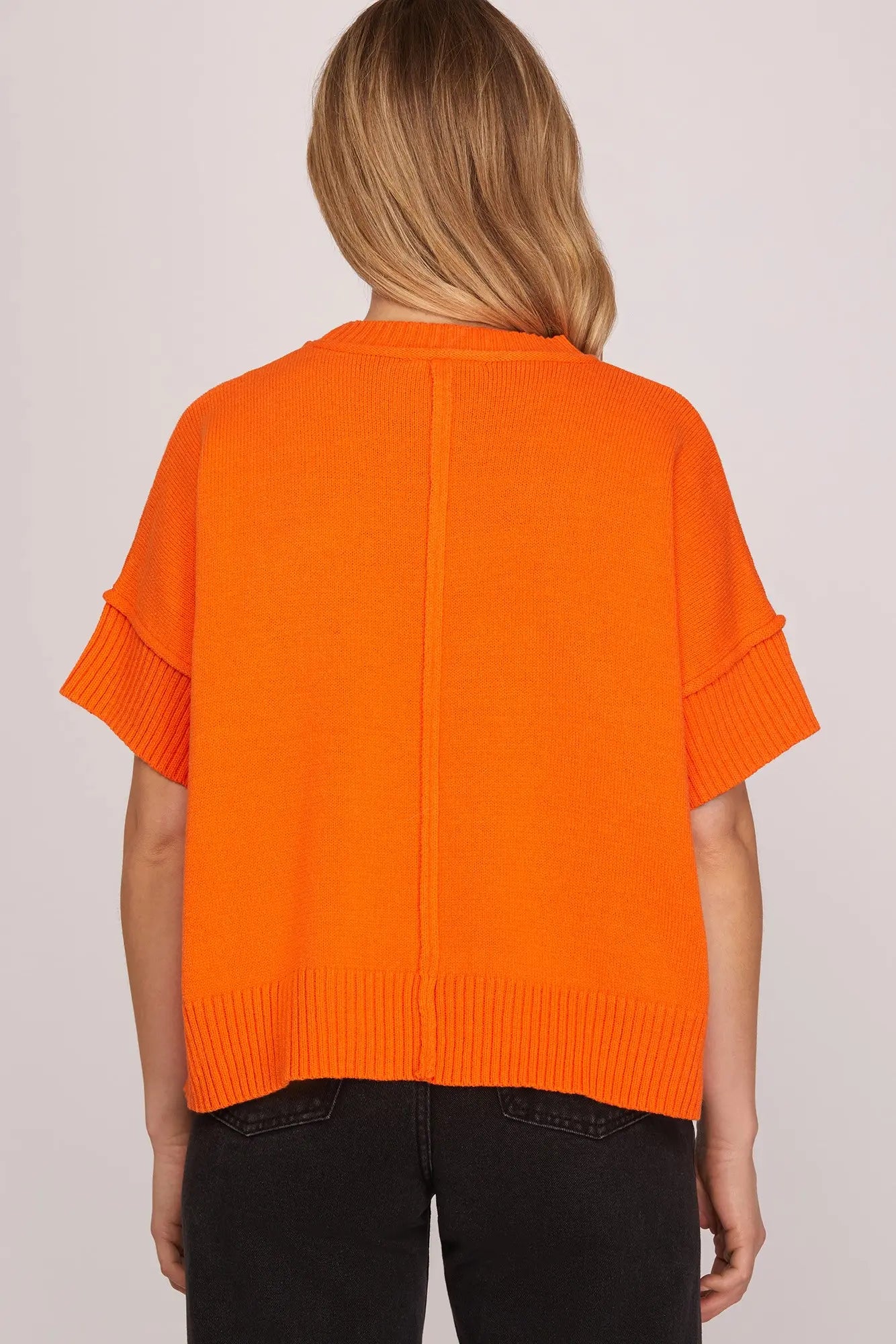 Person wearing an orange sweater on a plain background