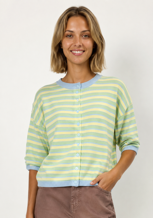 A woman with shoulder-length blonde hair wearing a pastel green and yellow striped cardigan with light blue ribbed trim, paired with brown pants, against a plain off-white background.
