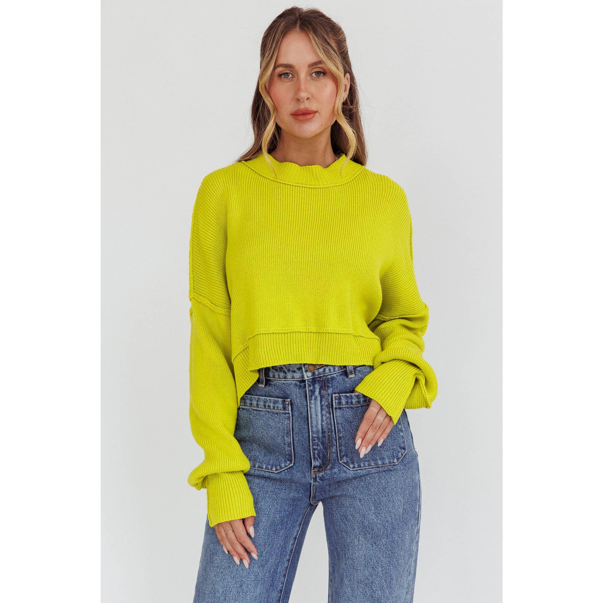 Woman wearing a bright yellow sweater and blue jeans on a light gray background